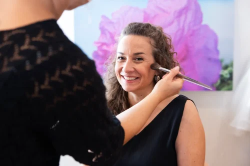 Frau erhält Make-up von Visagistin vor rosa Blume