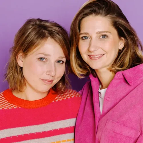 Zwei lächelnde Frauen vor einem lila Hintergrund