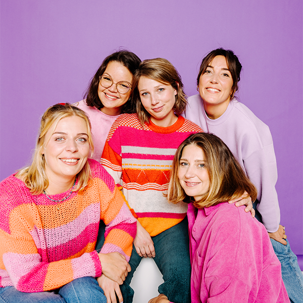 Fünf Frauen in bunten Pullovern vor lila Hintergrund