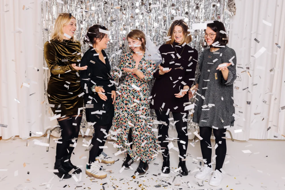 Fünf Frauen feiern mit Konfetti vor schimmerndem Hintergrund