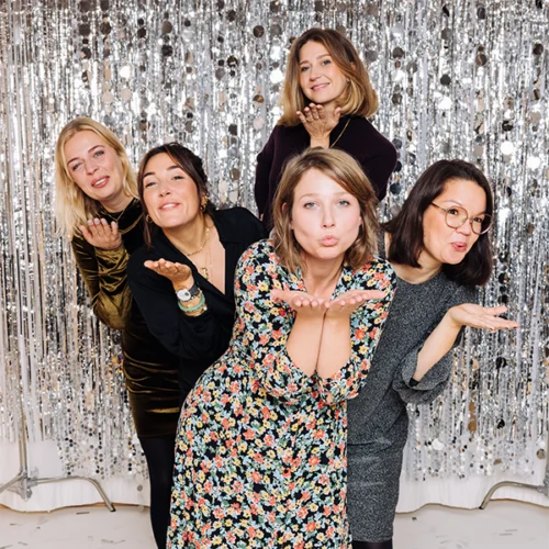 Fünf Frauen posieren vor silbernem Paillettenhintergrund