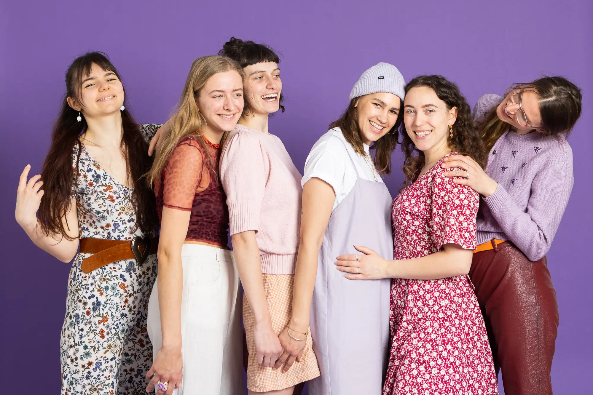 Sechs glückliche Frauen posieren gemeinsam vor lila Hintergrund