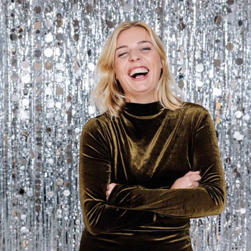 Frau in Samtkleid lacht vor glitzerndem Hintergrund