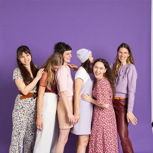 Gruppe von Frauen in bunter Kleidung vor lila Hintergrund